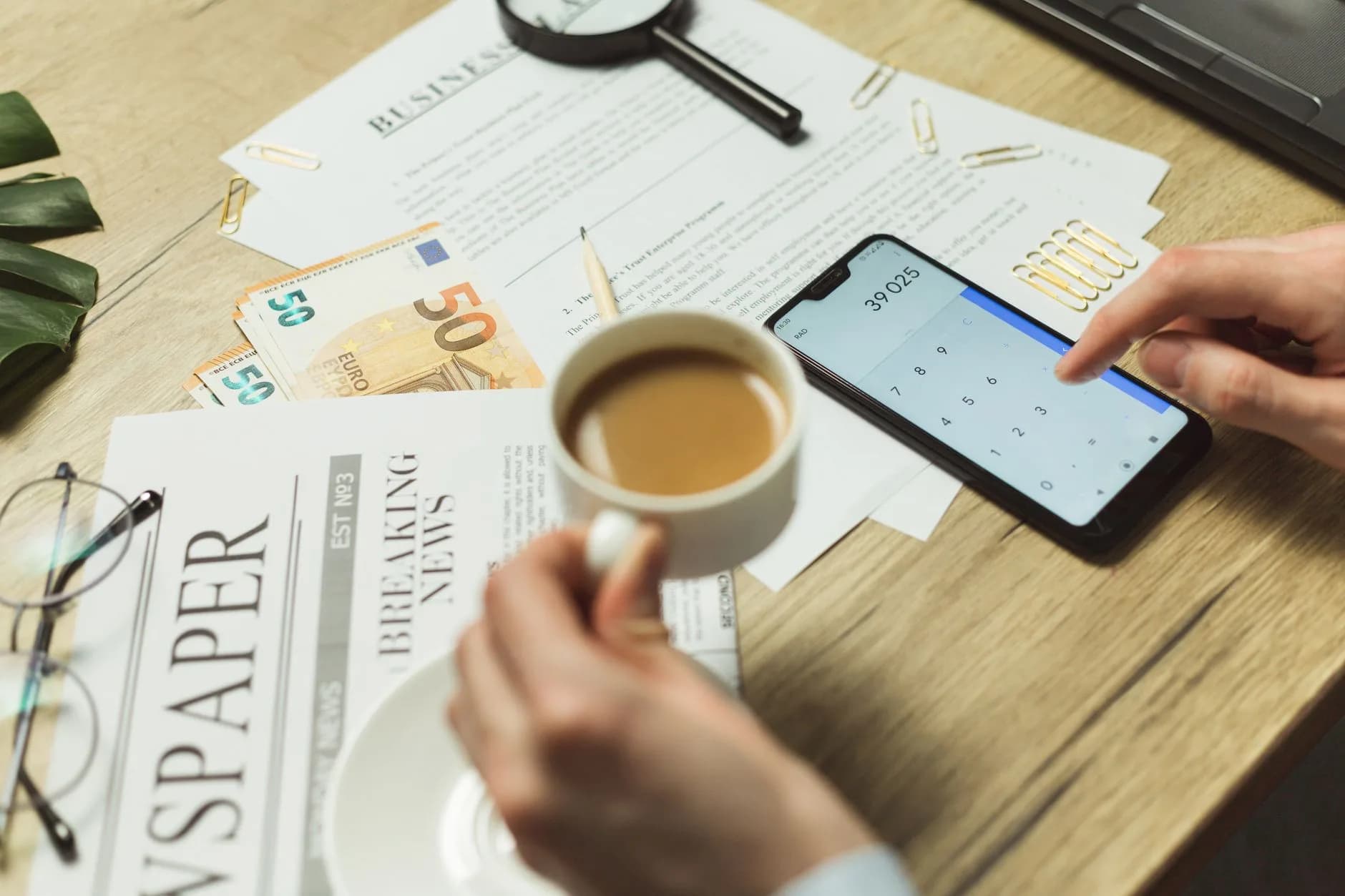 High-angle view of a business workspace with documents, coffee, currency, and smartphone calculator.