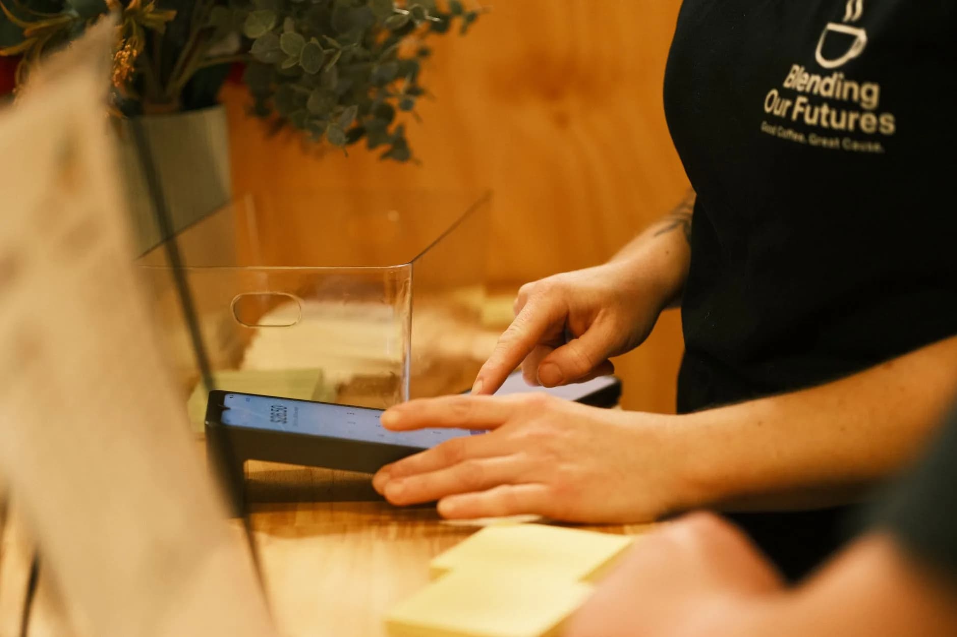 Barista interacting with a digital payment system in a cafe, highlighting modern technology in coffee shops.